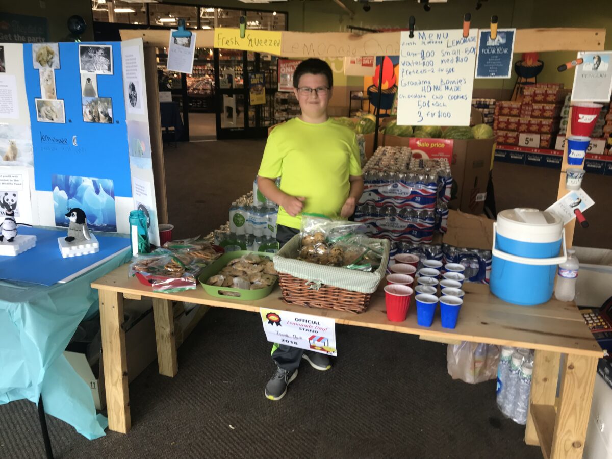 Young boy standing behind his official Lemonade Day stand inside Kroger grocery store